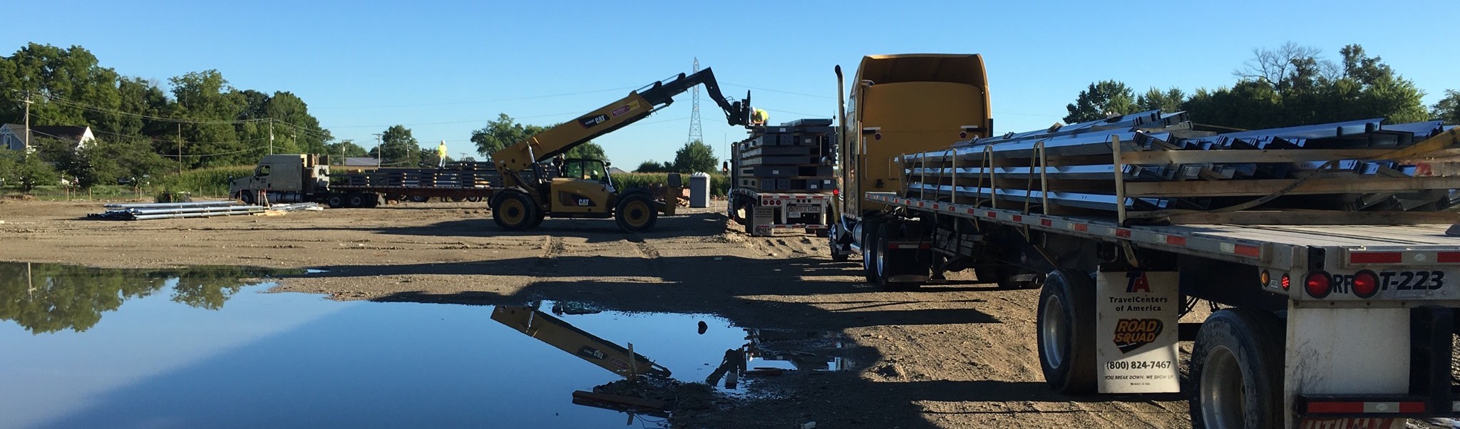 Flatbed trucks and telehandler delivering steel building materials to a construction site